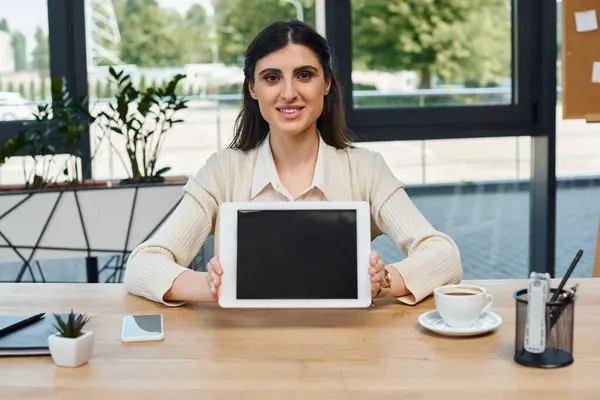 Una empresaria se sienta en una mesa elegante, comprometida con una tableta en la oficina moderna, una visión de emprendimiento e innovación. - foto de stock