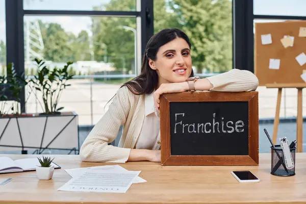 Eine Geschäftsfrau sitzt an einem modernen Schreibtisch und zeigt ein Schild als Symbol ihrer unternehmerischen Bemühungen.. — Stockfoto