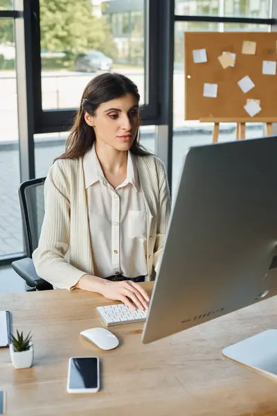 Una donna d'affari determinata siede alla sua scrivania in un ufficio moderno, completamente impegnata con il suo computer. — Foto stock