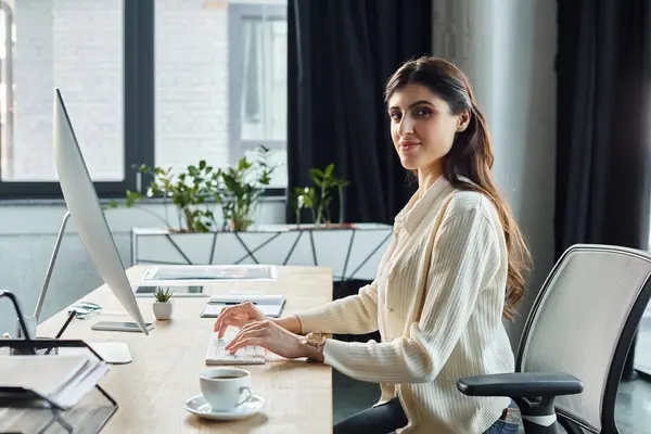 Une femme d'affaires assise à un bureau moderne, concentrée sur l'utilisation d'un ordinateur pour le travail numérique dans un bureau de franchise. — Photo de stock