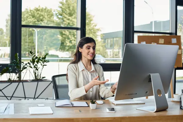 Una mujer de negocios está profundamente enfocada mientras está sentada en un escritorio con una computadora en un entorno de oficina moderno.. - foto de stock