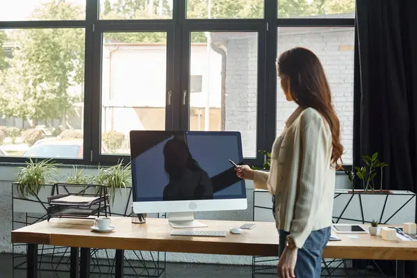 Une femme d'affaires se tient en confiance devant un écran d'ordinateur dans un bureau moderne, immergée dans le monde des concepts de franchise. — Photo de stock