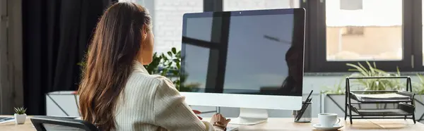 Uma empresária sentada atrás de uma mesa, trabalhando em um computador em um ambiente de escritório moderno. — Fotografia de Stock
