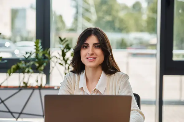 Une femme d'affaires se concentre intensément, assise devant un ordinateur portable dans un bureau moderne, incarnant détermination et engagement. — Photo de stock