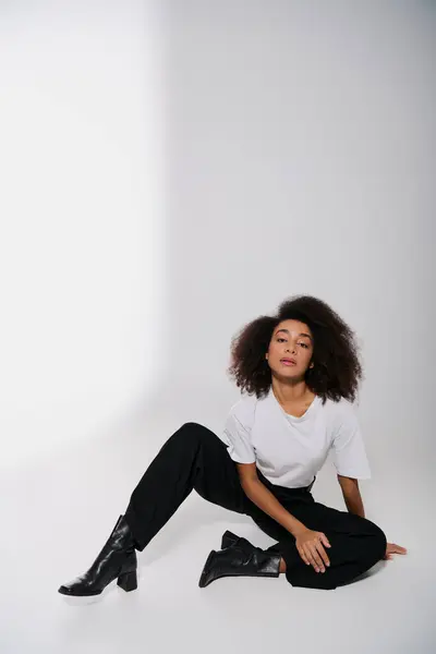 Buen aspecto afroamericano modelo femenino sentado en el suelo y mirando a la cámara, concepto de moda - foto de stock