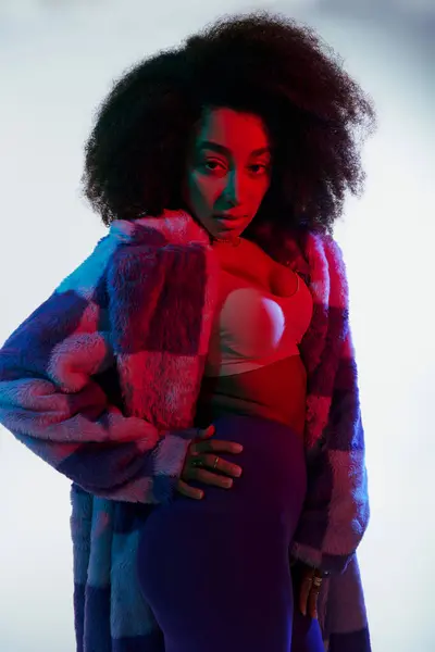 Debonair african american woman in vibrant faux fur with curly hair looking at camera in lights — Stock Photo