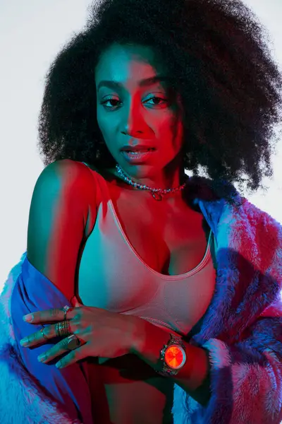 Sexy Africano americano mulher no sutiã e peles falsas olhando para a câmera cercada por luzes vermelhas e azuis — Fotografia de Stock