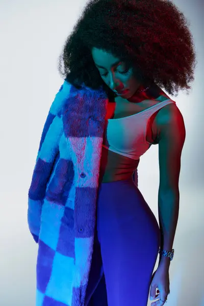 Alluring stylish african american female model in fashionable faux fur looking way in lights — Stock Photo
