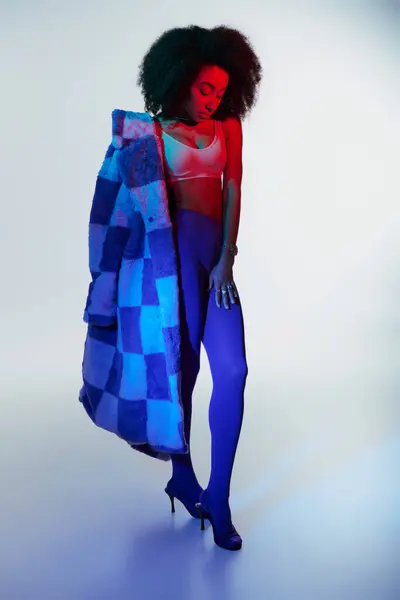 Sedutor elegante modelo feminino afro-americano na moda peles falsas olhando maneira em luzes — Fotografia de Stock