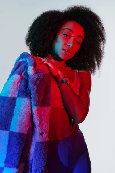 Beautiful sexy african american woman in fashionable stylish faux fur looking at camera in lights — Stock Photo