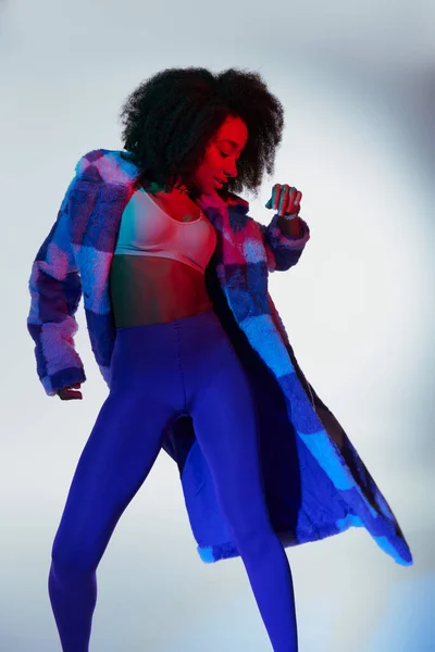 Séduisante modèle féminin afro-américain élégant en fausse fourrure à la mode dans les lumières — Photo de stock