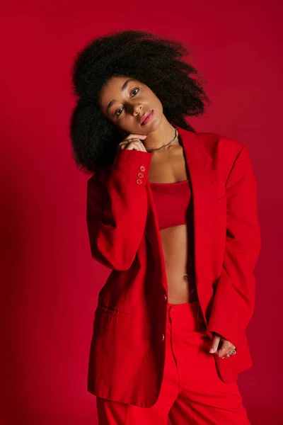Attraente seducente donna afro-americana in abiti vibranti guardando la fotocamera su sfondo rosso — Foto stock