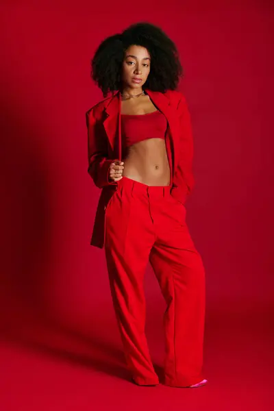 Atraente sedutor mulher afro-americana em trajes vibrantes olhando para a câmera no fundo vermelho — Fotografia de Stock