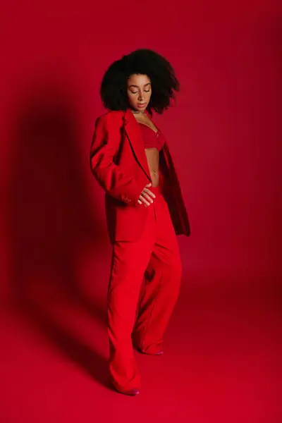 Sexy donna afroamericana in abito rosso elegante guardando altrove su sfondo rosso, concetto di moda — Foto stock