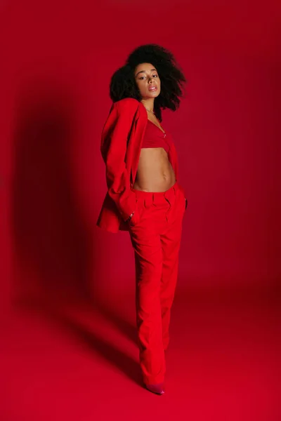 Attraente seducente donna africana americana in abiti vibranti guardando la fotocamera sullo sfondo rosso — Foto stock