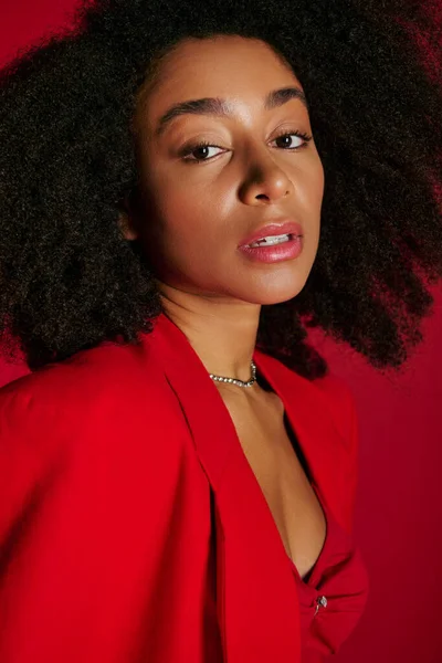Приваблива афроамериканська жінка в яскравому вбранні дивиться на камеру на червоному тлі — стокове фото