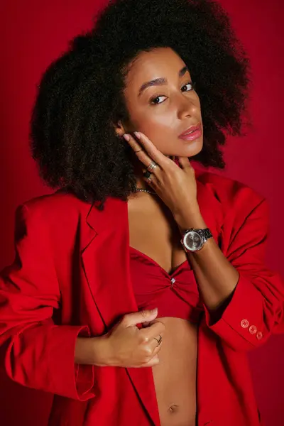 Good looking alluring african american woman in vibrant attire looking at camera on red backdrop — Stock Photo