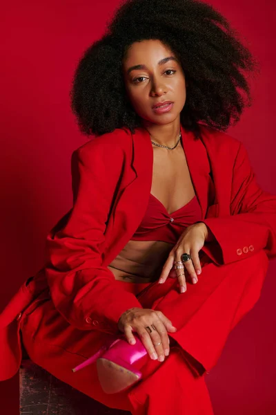 Bela mulher americana africana sexy em traje vermelho sentado e olhando para a câmera, conceito de moda — Fotografia de Stock