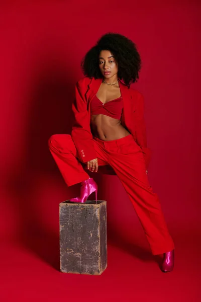 Modello femminile afro-americano piuttosto alla moda in abbigliamento sexy guardando la fotocamera su sfondo rosso — Foto stock