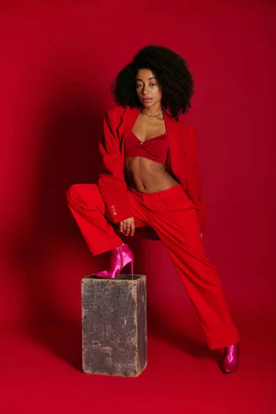 Pretty fashionable african american female model in sexy attire looking at camera on red background — Stock Photo