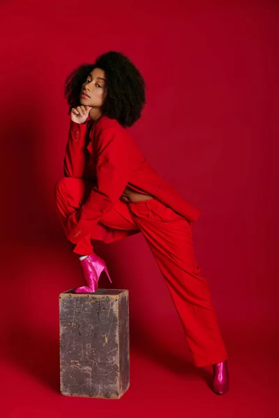 Modello femminile afro-americano piuttosto alla moda in abbigliamento sexy guardando la fotocamera su sfondo rosso — Foto stock