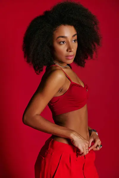 Sexy sedutor mulher afro-americana em sutiã vibrante vermelho posando no fundo vermelho e olhando para longe — Fotografia de Stock
