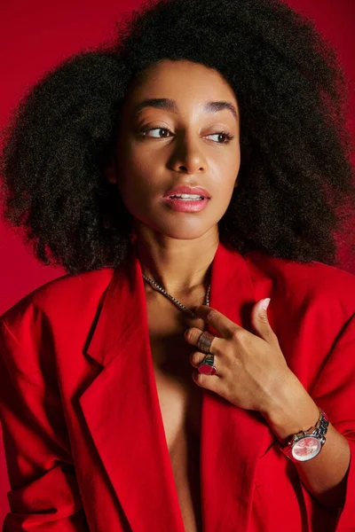 Alluring african american female model in red blazer looking away on red background, fashion concept — Stock Photo