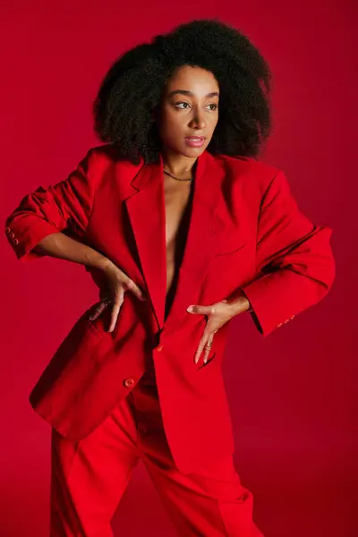 Seductora modelo femenina afroamericana en chaqueta roja mirando hacia otro lado sobre fondo rojo, concepto de moda - foto de stock