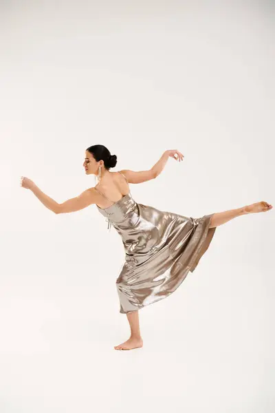 Eine junge Frau in einem silbernen Kleid tanzt anmutig in einem Studio vor weißem Hintergrund. — Stockfoto
