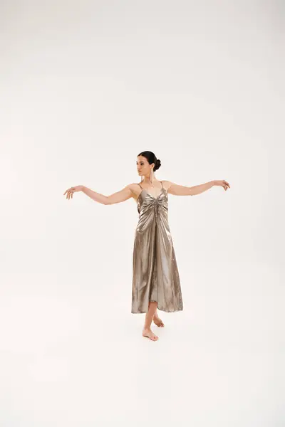 Uma jovem mulher em um vestido de prata dança graciosamente, expressando elegância e movimento em um estúdio contra um pano de fundo branco. — Fotografia de Stock