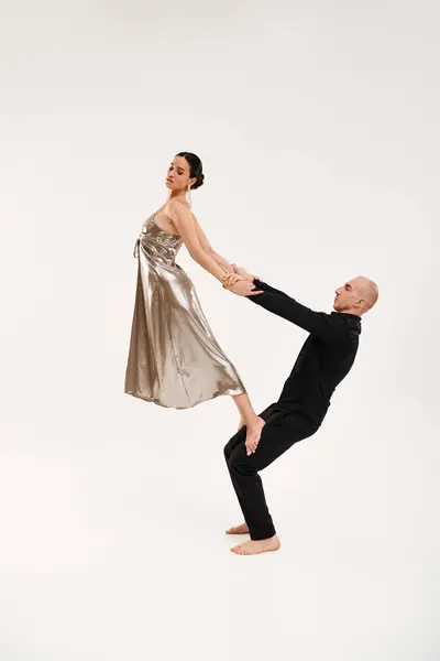 Um jovem de preto e uma mulher de vestido de prata realizam movimentos acrobáticos de dança juntos contra um fundo de estúdio branco. — Fotografia de Stock