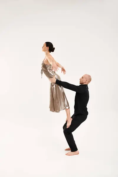 Jeune homme et femme vêtus de noir exécutant des mouvements de danse acrobatique sur un plancher blanc dans un cadre de studio. — Photo de stock
