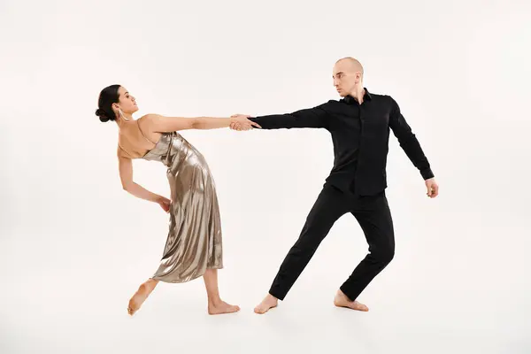 A young man in black and a young woman in a shiny silver dress showcasing acrobatic dance moves in a studio against a white background. — Stock Photo