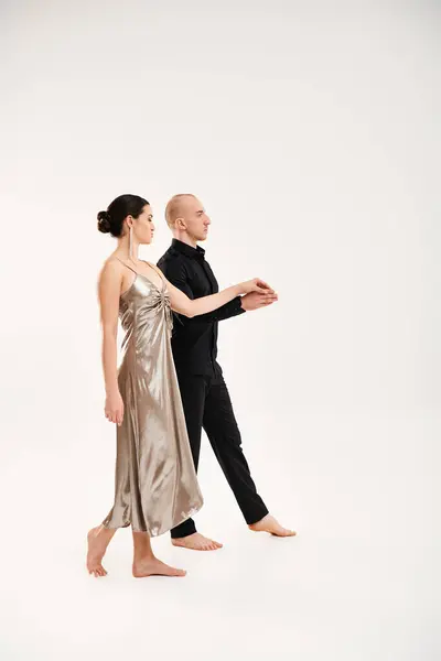 Un joven de negro y una joven con un vestido plateado bailan juntos en un estudio sobre un fondo blanco. - foto de stock