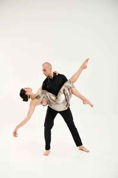 Молодий чоловік в чорному і молода жінка в срібному блискучому платті танцюють разом, виконуючи акробатичні елементи в студії на білому тлі. — стокове фото