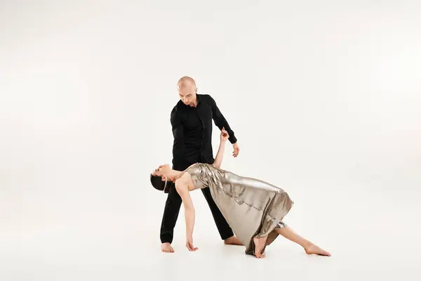 Un giovane in nero e una giovane donna in abito danzano in coppia, incorporando elementi acrobatici. Studio girato su uno sfondo bianco. — Foto stock