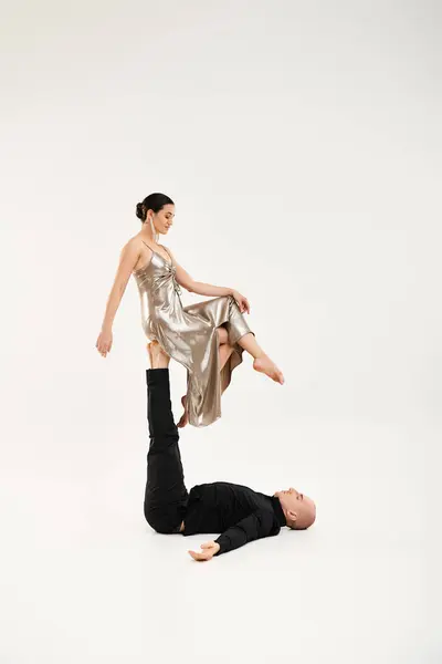 A young man in black and a young woman in a shiny dress performing an acrobatic dance routine in a studio against a white background. — Stock Photo