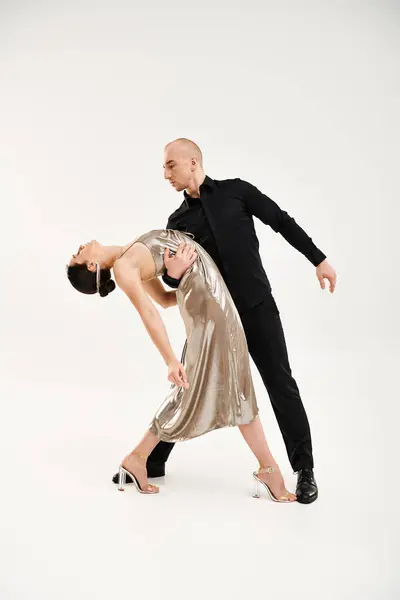 Un jeune homme en noir et une jeune femme en robe brillante exécutent ensemble une danse acrobatique sur fond de studio blanc. — Photo de stock