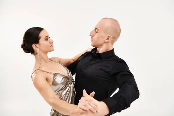 A young man in black and a young woman in a shiny dress dance together in a studio setting with a white background. — Stock Photo