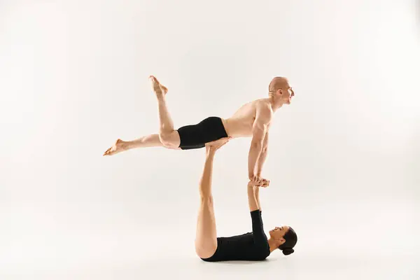 Un joven sin camisa realiza una parada de manos encima de otra mujer, ambas dedicadas a una hazaña acrobática en un entorno de estudio. - foto de stock