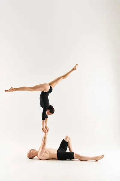 A shirtless young man and a young woman gracefully performing a handstand together in a studio setting against a white background. — Stock Photo