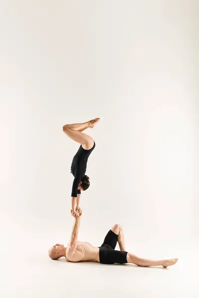 Un giovane uomo senza maglietta e una donna eseguono una postazione, mettendo in mostra le loro abilità acrobatiche in uno studio ambientato su uno sfondo bianco. — Foto stock