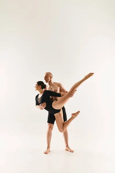 Un joven sin camisa y una joven con gracia realizan elementos acrobáticos en un estudio sobre un fondo blanco. - foto de stock