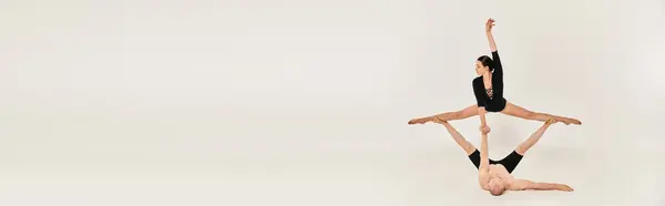 Un joven sin camisa y una joven bailarina interpretando elementos acrobáticos mientras está de pie en el aire sobre un fondo blanco. - foto de stock