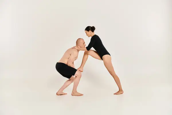 Un hombre joven sin camisa y una mujer joven bailan en pareja, ejecutando elementos acrobáticos en un estudio filmado sobre un fondo blanco. - foto de stock