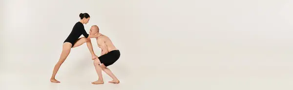 Un joven sin camisa y una joven bailarina muestran juntos elementos acrobáticos en un estudio rodado sobre un fondo blanco. - foto de stock