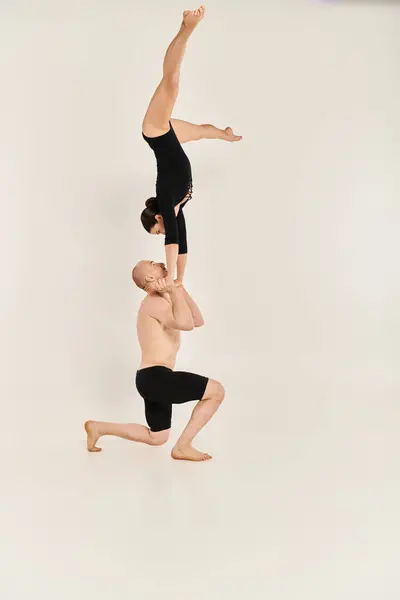 Young shirtless man and woman execute a flawless handstand in mid-air against a white studio backdrop. — Stock Photo