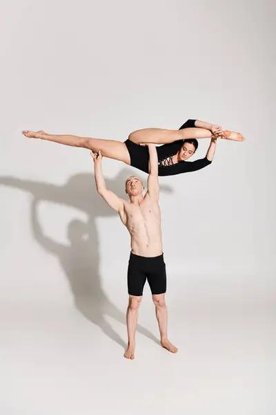 A shirtless young man and a young woman perform a handstand as part of an acrobatic dance routine in a studio setting. — Stock Photo