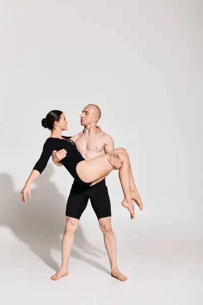 Un giovane uomo senza maglietta tiene una donna in una posa acrobatica di danza, mostrando forza e grazia in uno studio ambientato su uno sfondo bianco. — Foto stock