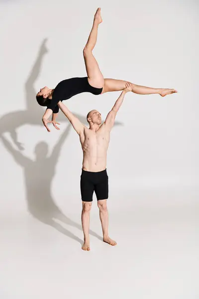 Young shirtless man holding a young woman, showcasing agility and balance in a studio setting against a white background. — Stock Photo